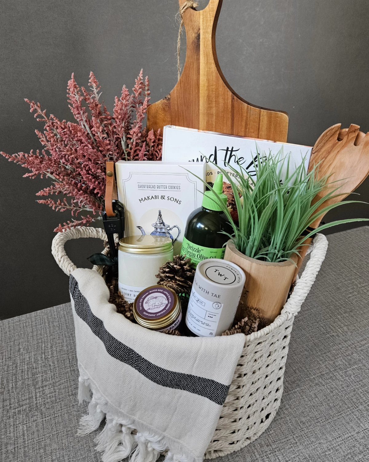 White woven basket filled with home decor items, a plant, and dried flowers.
