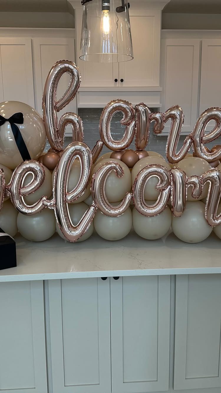 Rose gold welcome home foil balloons resting on white balloons on a counter