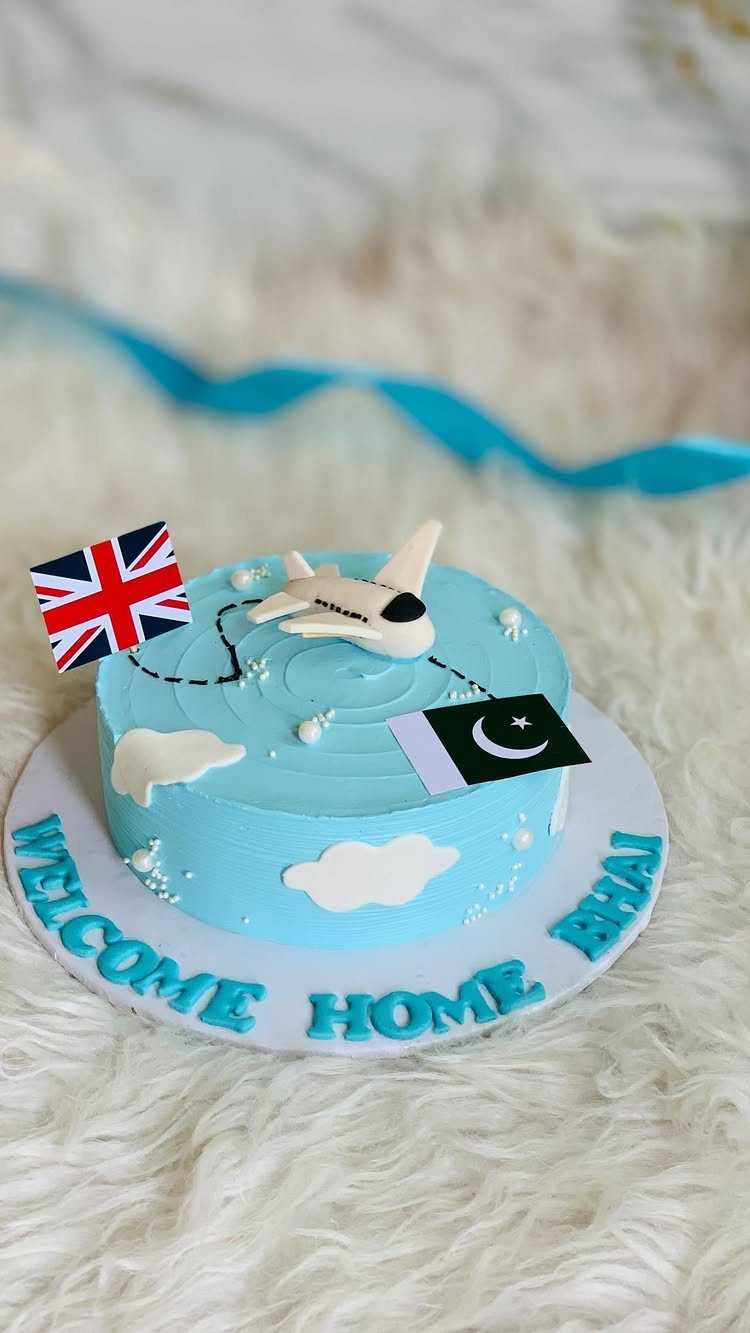 Blue welcome home cake with airplane, UK and Pakistan flags, and text.