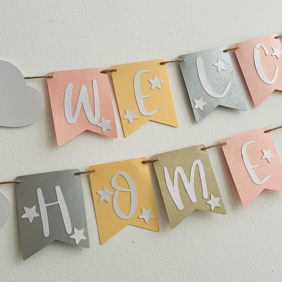 Colorful paper banner spelling Welcome Home with stars on a white wall