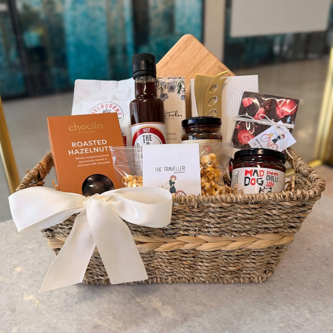 Woven wicker gift basket filled with gourmet foods and tied with a white bow.