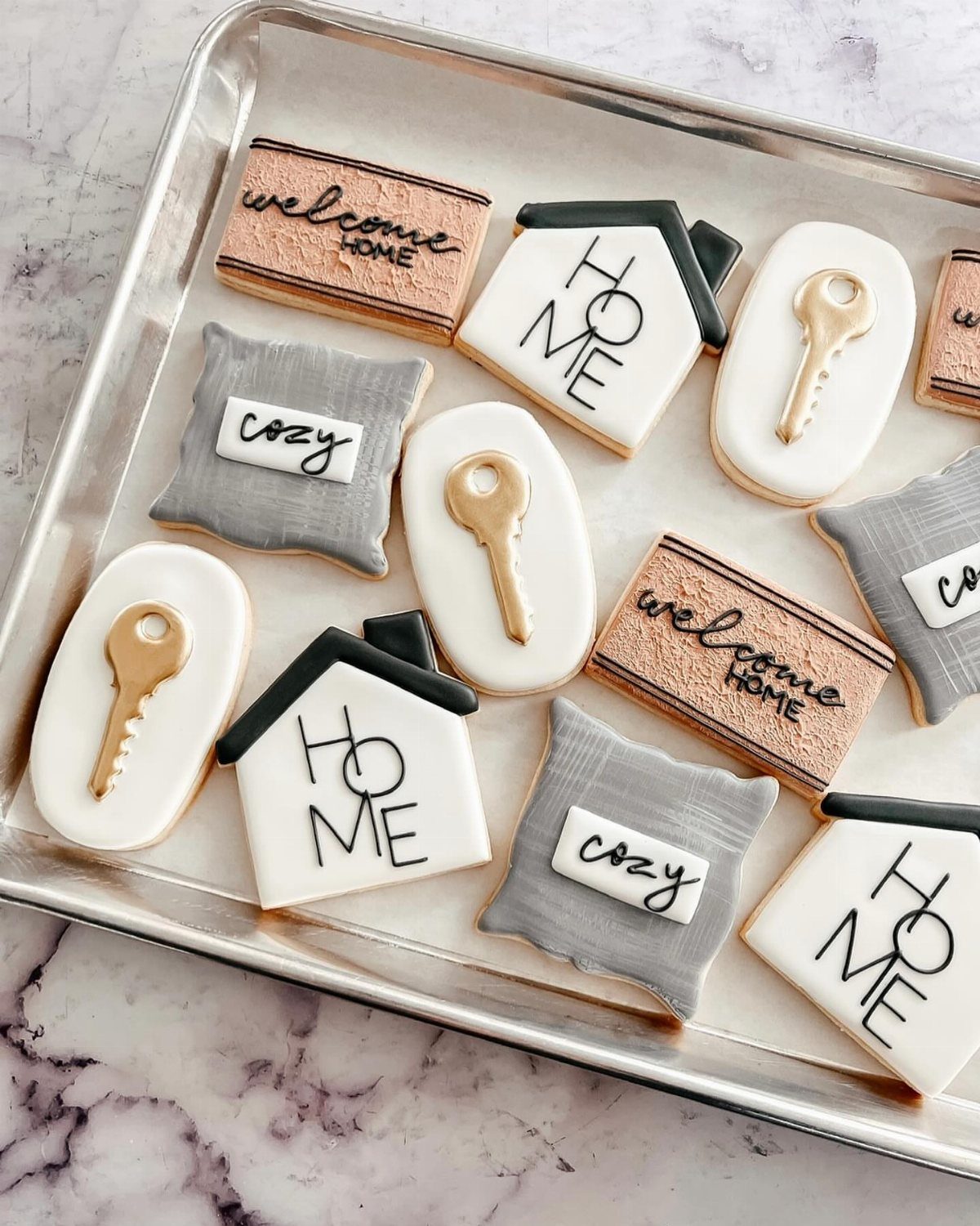 Decorated sugar cookies shaped like houses and keys on a silver baking tray.