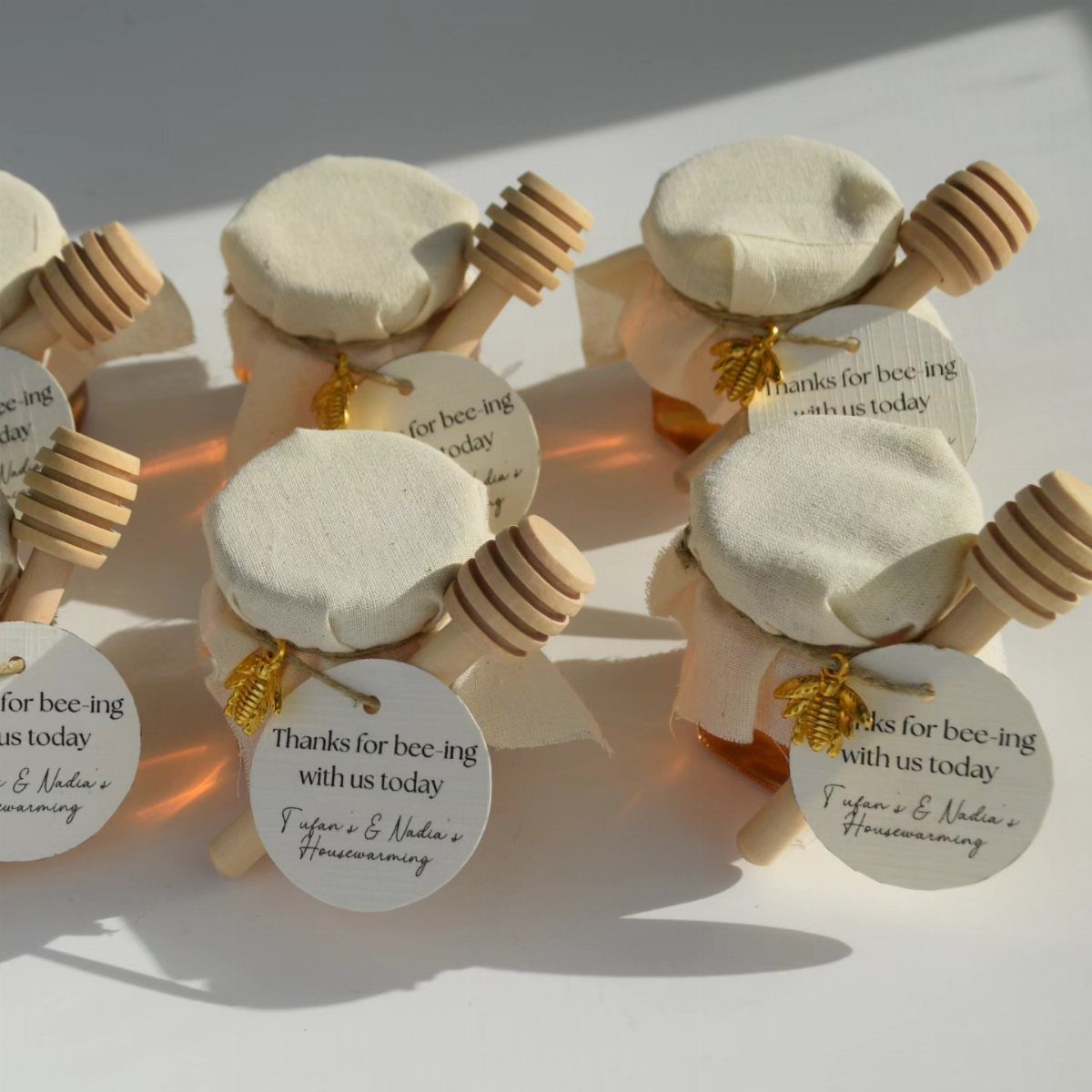 Small honey jars with fabric lids, wooden dippers, and personalized thank you tags.