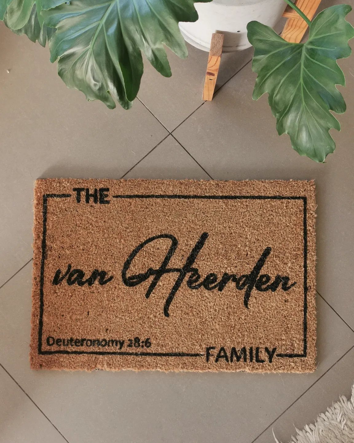 Personalized coir welcome mat with family name on a grey tiled floor.