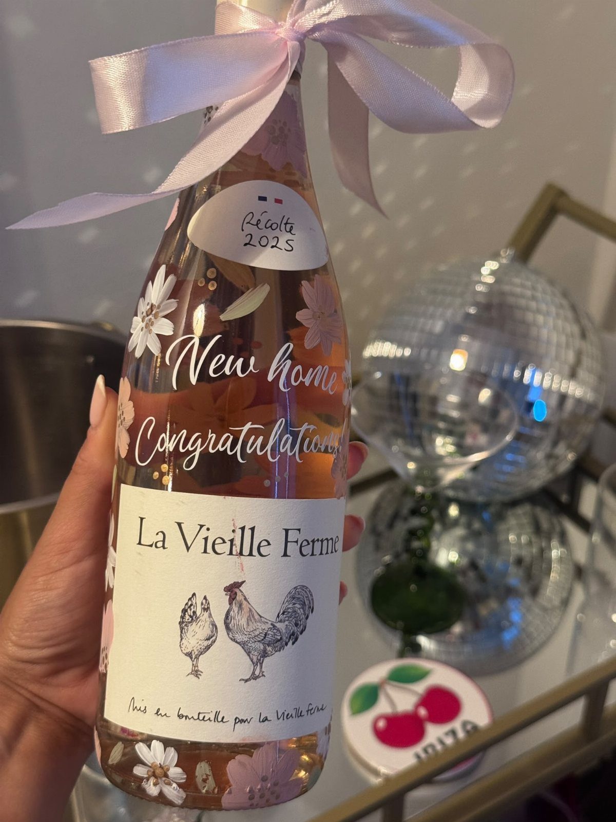 Bottle of rosé wine with a pink ribbon and floral label for housewarming.