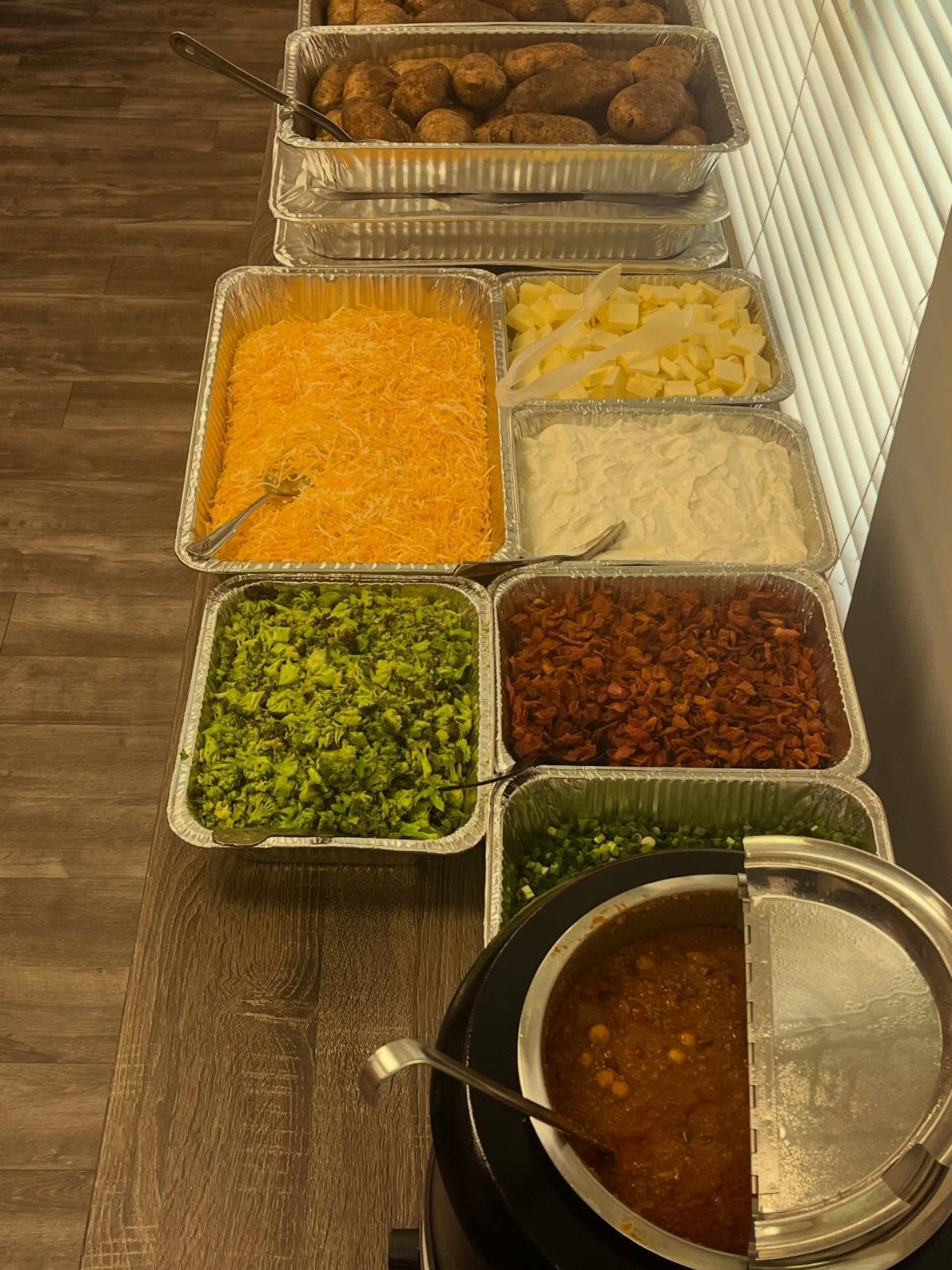 Baked potato bar with various toppings including cheese, broccoli, bacon, and chili.