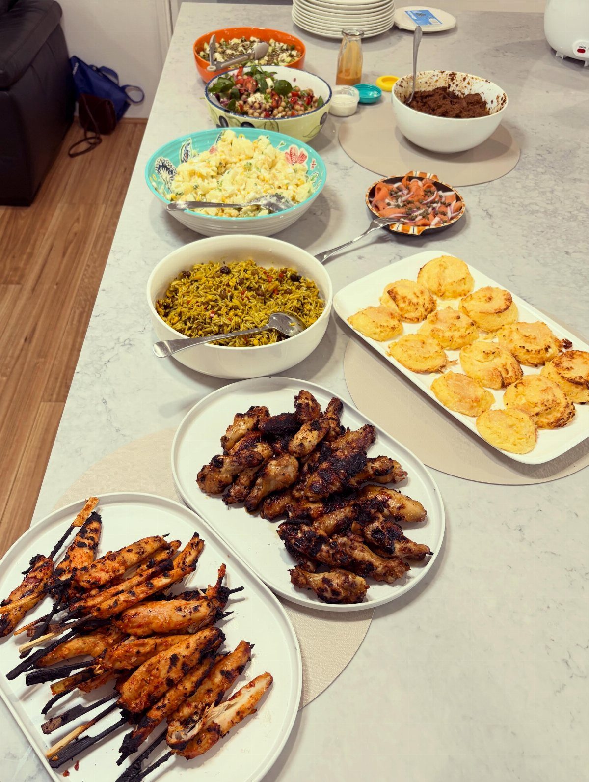 Grilled chicken skewers and wings with side dishes on a white table.
