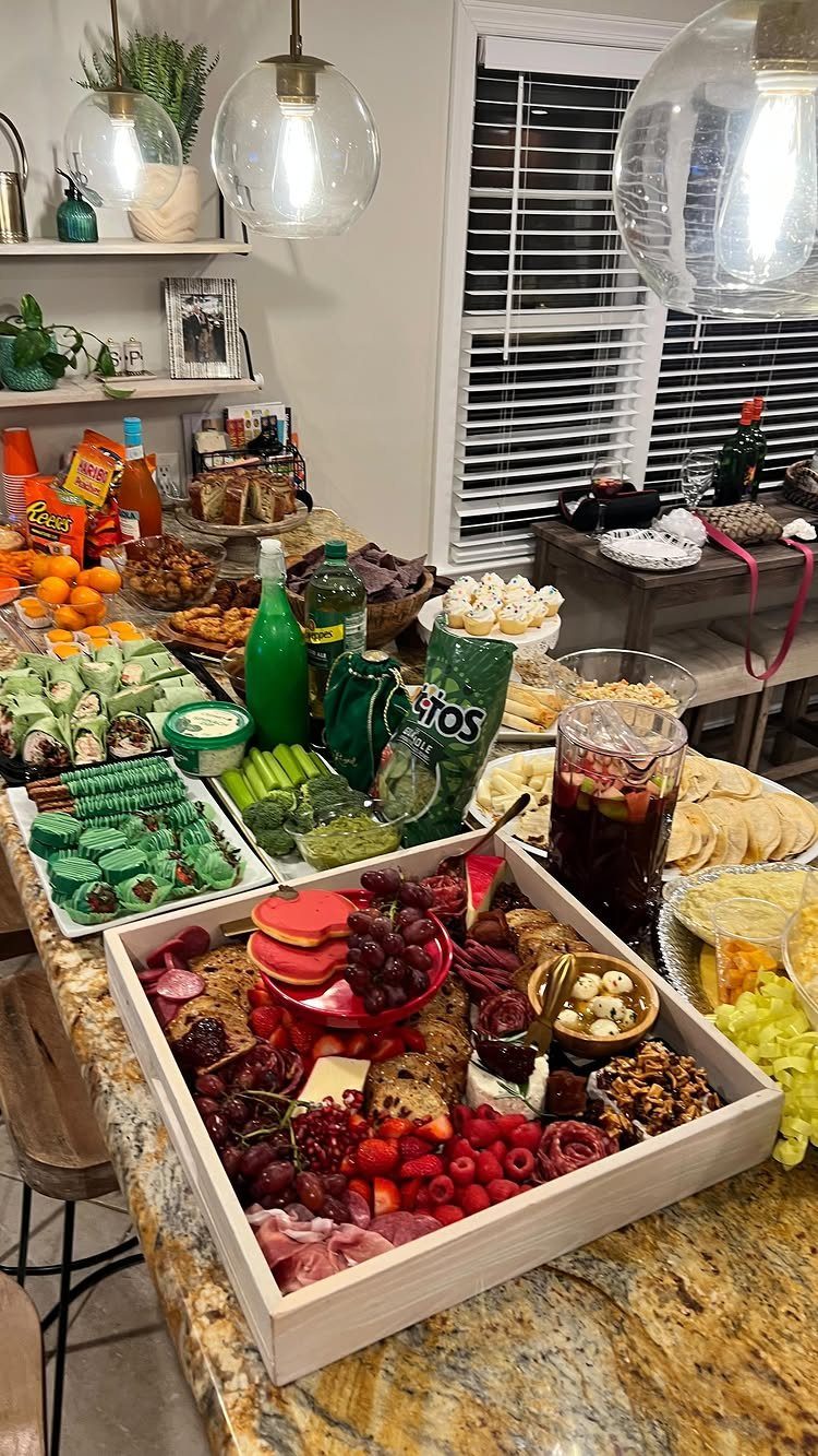 Assorted party platters including a red-themed charcuterie board and green appetizers on a counter.