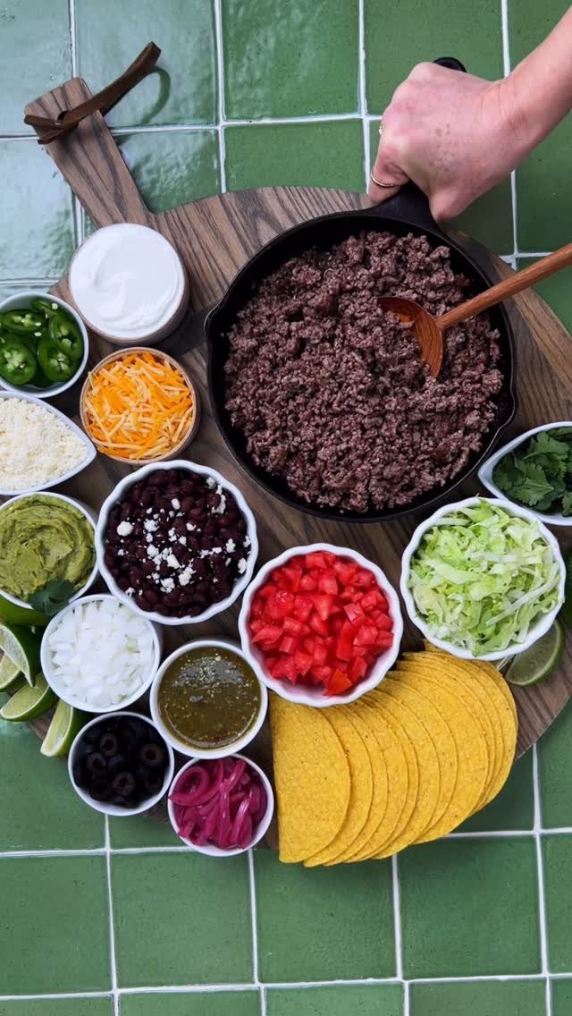 Taco bar setup with ground meat, taco shells, and various colorful toppings.