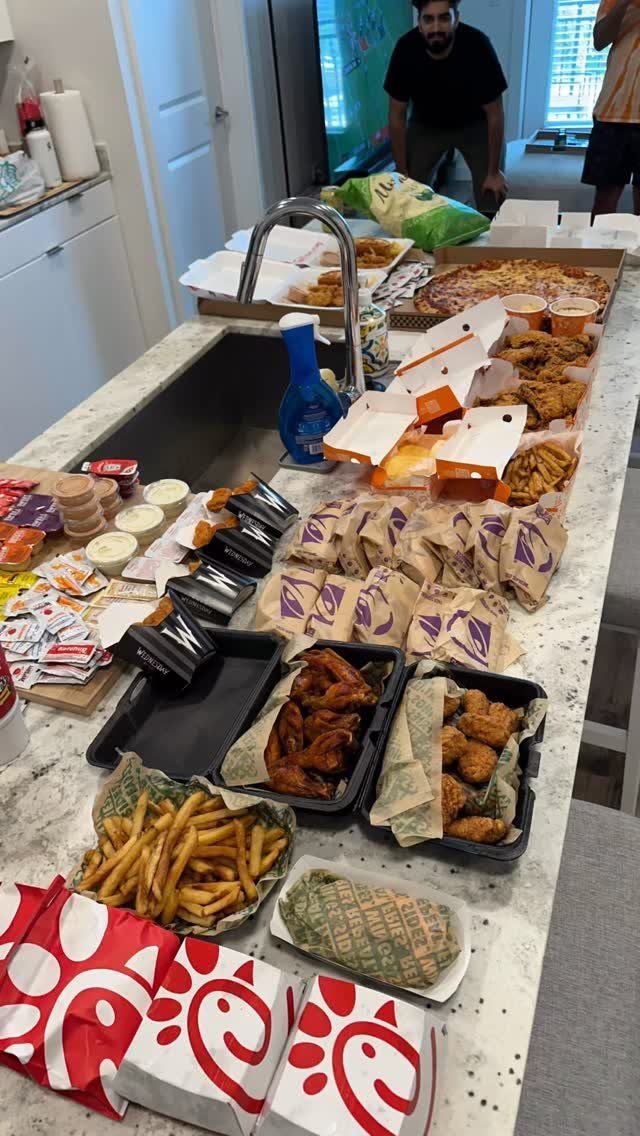 Takeout fried chicken, fries, and pizza spread across a white kitchen counter.
