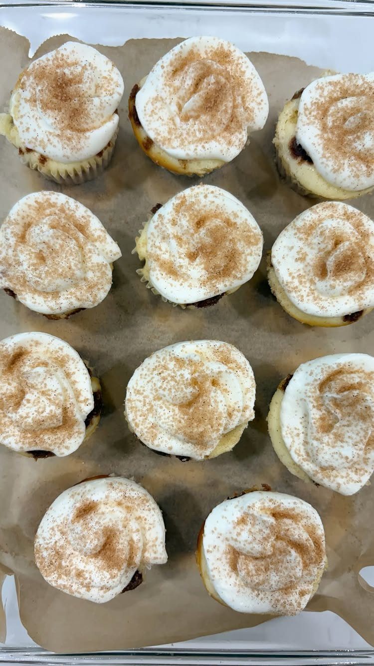 Mini cupcakes with white frosting and cinnamon powder on a baking tray.