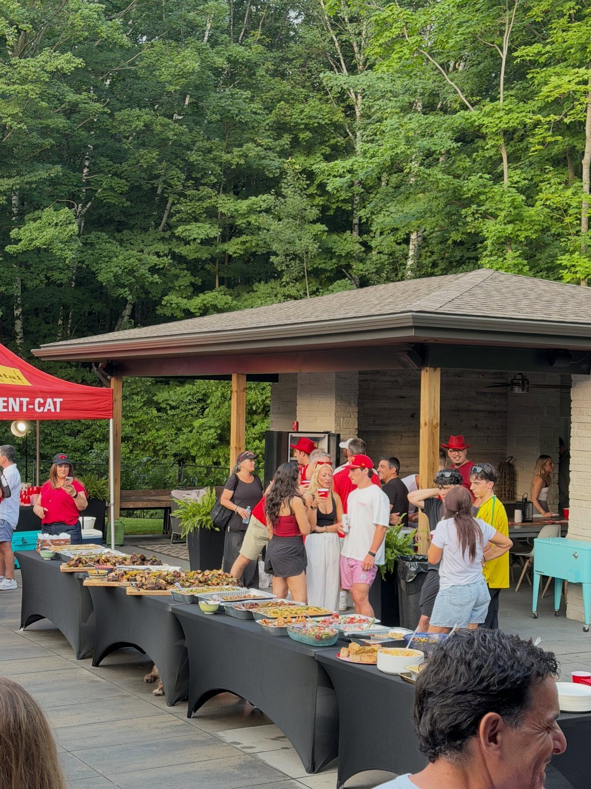 People gathering around long tables of food at an outdoor potluck event.