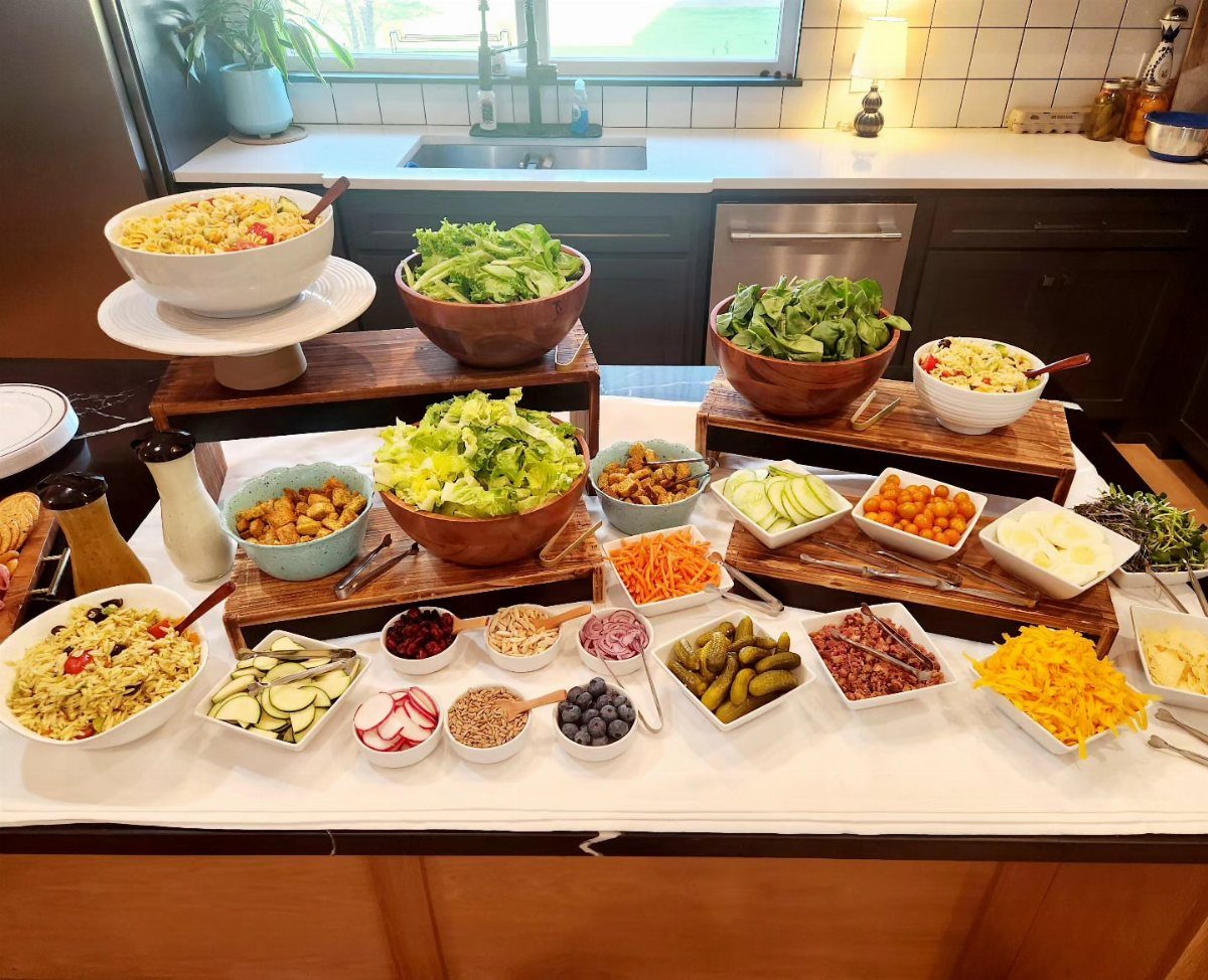 Salad bar with various bowls of greens, vegetables, and grains on a table.