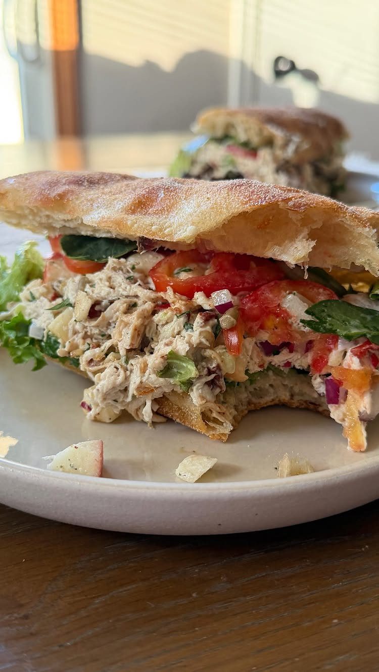 Chicken salad sandwiches with fresh vegetables on a white plate and wooden table.