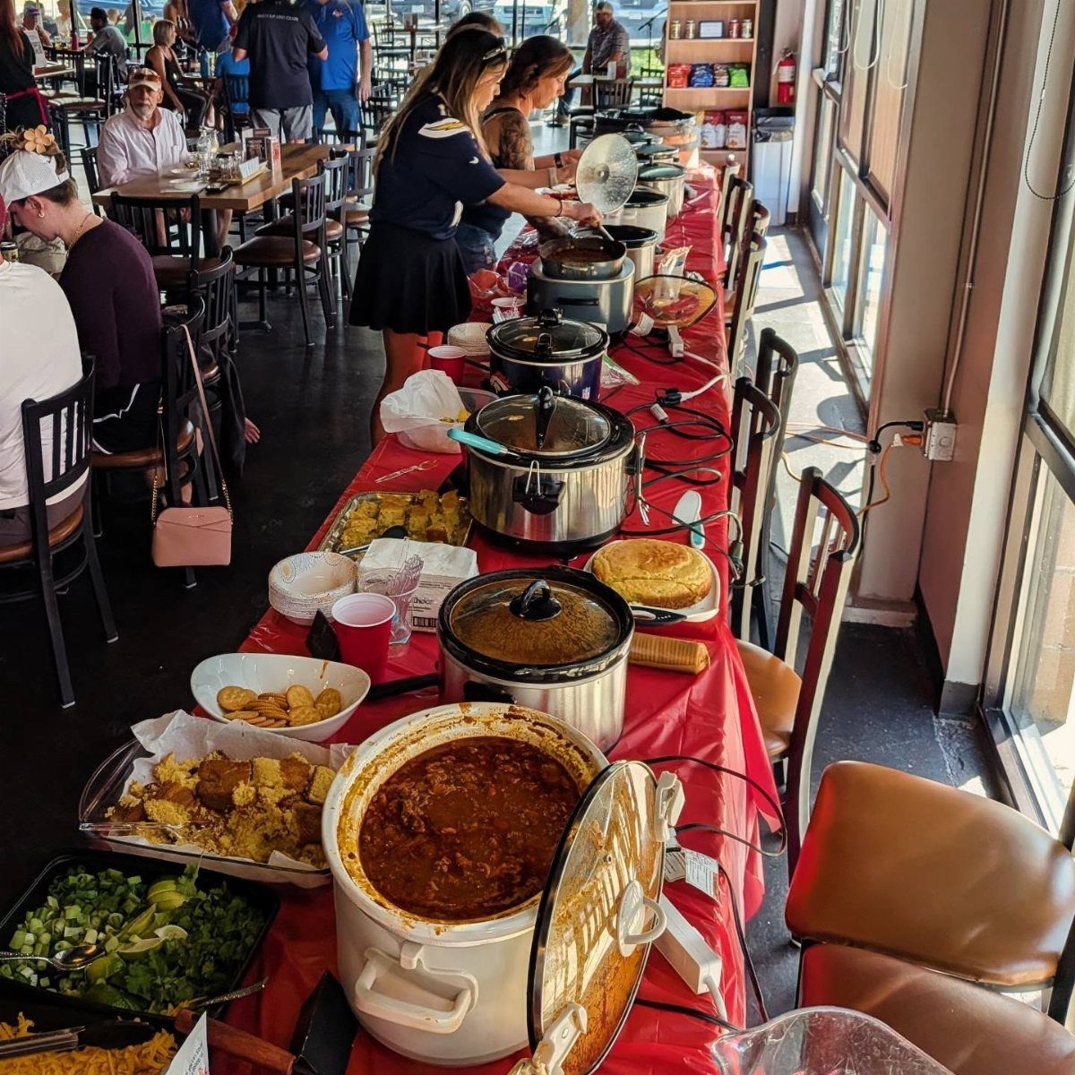 Slow cookers filled with chili and soup on a red tablecloth buffet table.